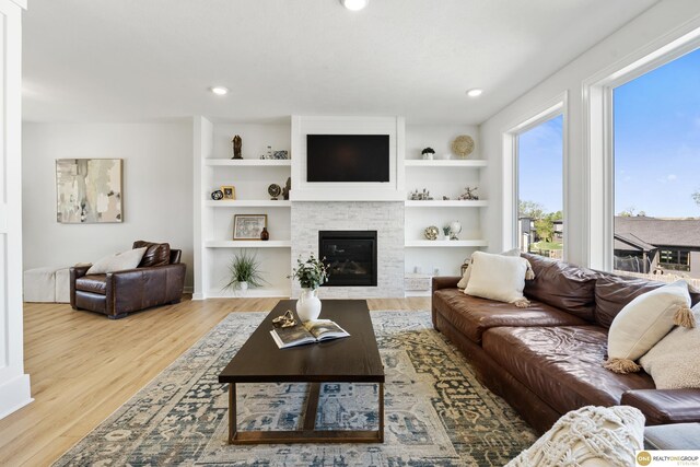 living room featuring a glass covered fireplace, built in features, recessed lighting, and wood finished floors