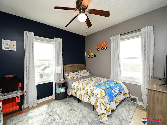 bedroom with ceiling fan, visible vents, and wood finished floors