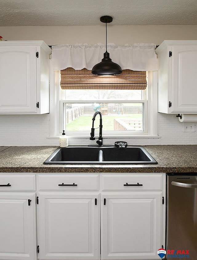 kitchen featuring white cabinets, dark countertops, a sink, decorative backsplash, and stainless steel dishwasher