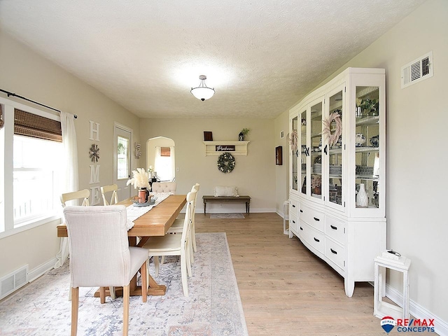 dining space with visible vents, arched walkways, light wood-style floors, and a textured ceiling