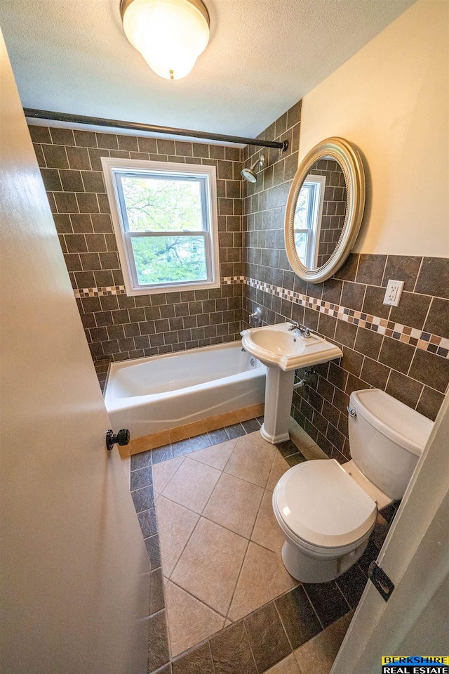 full bath with shower / bath combination, tile patterned floors, toilet, and tile walls
