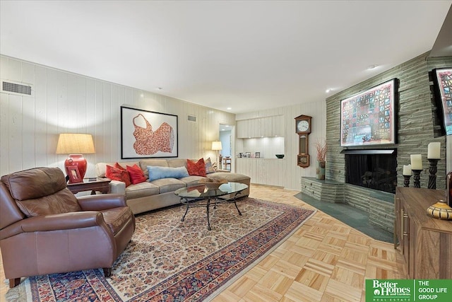 living area featuring wooden walls, visible vents, and a stone fireplace