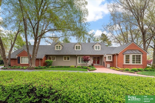 cape cod-style house featuring roof with shingles, a front lawn, and brick siding