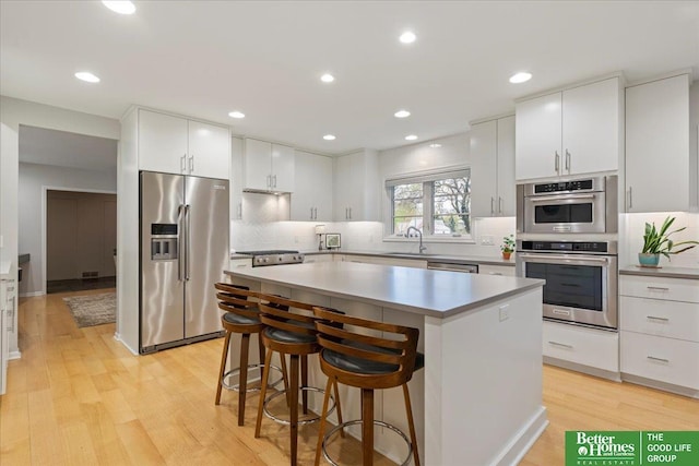 kitchen featuring a sink, light wood-style floors, a center island, stainless steel appliances, and backsplash