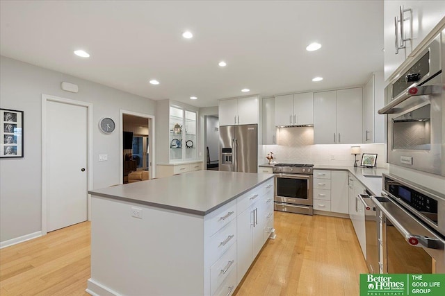kitchen featuring decorative backsplash, a center island, white cabinetry, light wood finished floors, and stainless steel appliances