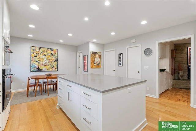 kitchen with stainless steel oven, a center island, white cabinetry, baseboards, and light wood-type flooring