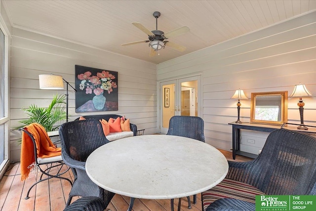 dining space with wood-type flooring, a ceiling fan, and wooden walls