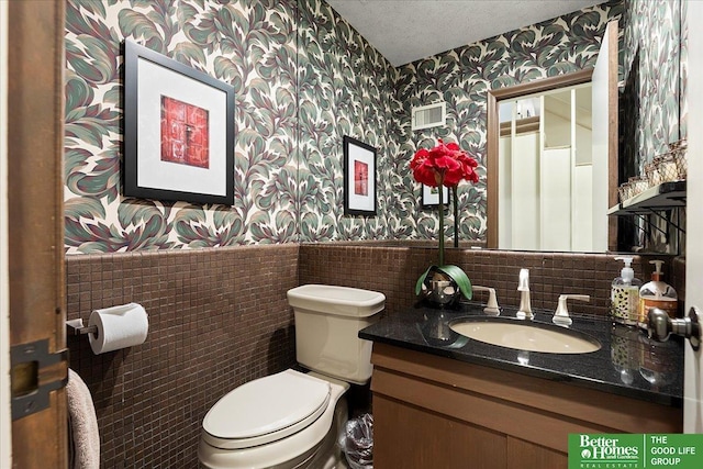 bathroom with vanity, wainscoting, wallpapered walls, and toilet