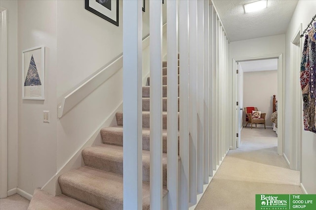 staircase featuring carpet floors, a textured ceiling, and baseboards
