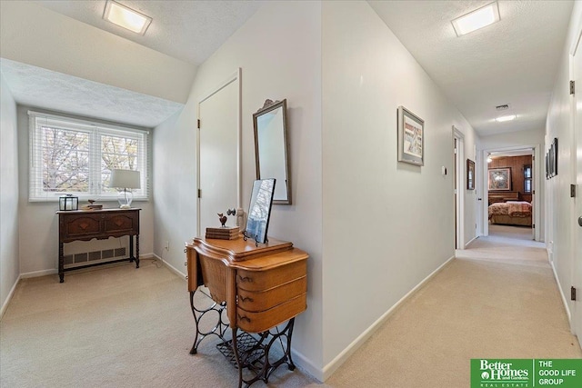 hallway with a textured ceiling, visible vents, light carpet, and baseboards