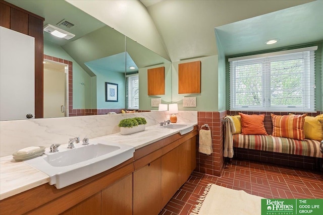 full bath featuring a sink, double vanity, brick patterned floor, a shower stall, and lofted ceiling