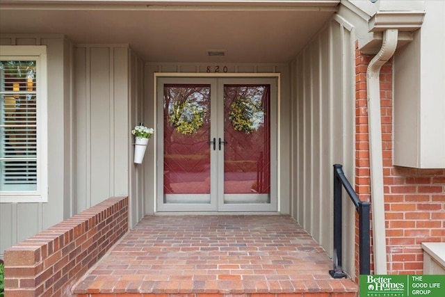 view of exterior entry with french doors, board and batten siding, visible vents, and brick siding