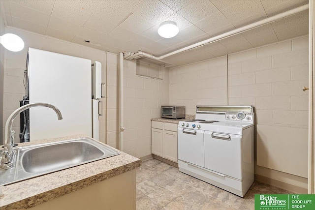 kitchen with white appliances, concrete block wall, a sink, and light countertops