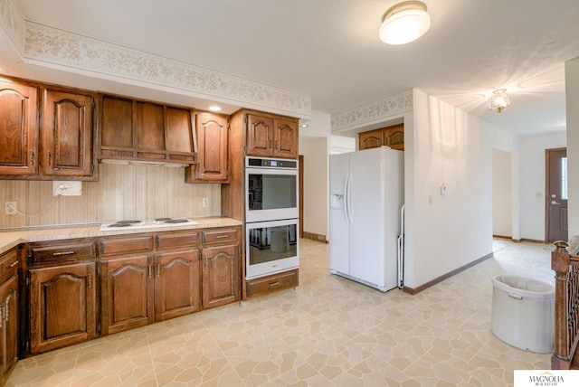 kitchen with white appliances, light countertops, brown cabinets, tasteful backsplash, and stone finish flooring