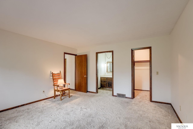 unfurnished bedroom featuring a walk in closet, visible vents, baseboards, and light colored carpet