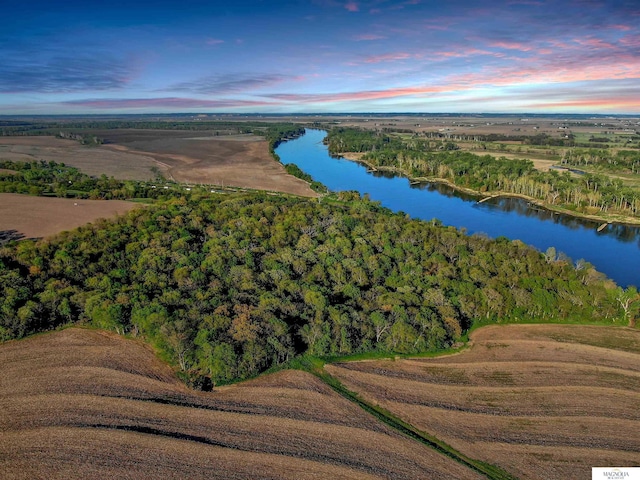 aerial view at dusk with a water view and a view of trees