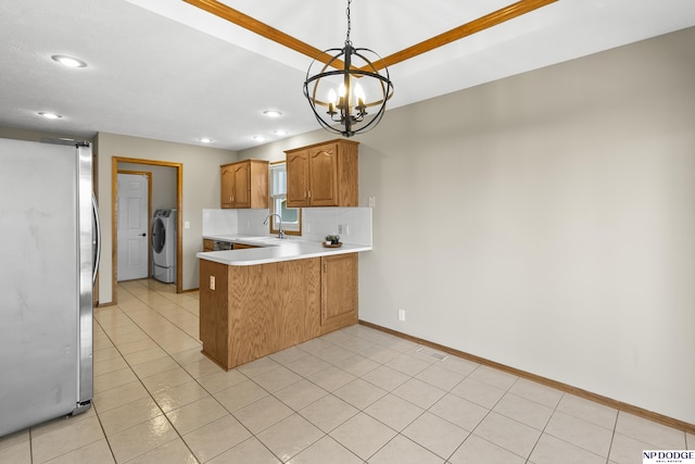 kitchen with a sink, light countertops, freestanding refrigerator, a peninsula, and a notable chandelier