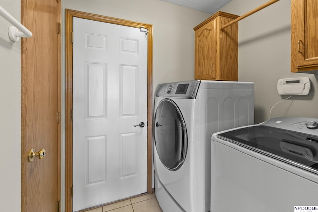 washroom featuring cabinet space, light tile patterned flooring, and washing machine and clothes dryer