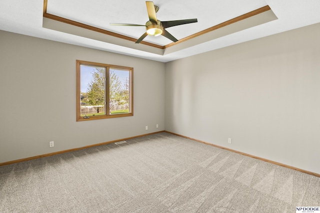 empty room featuring visible vents, a ceiling fan, carpet, and a tray ceiling