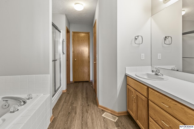 bathroom featuring a bath, visible vents, a stall shower, wood finished floors, and vanity