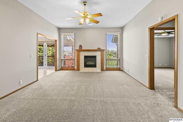 unfurnished living room with carpet floors, a ceiling fan, a wealth of natural light, and a tile fireplace