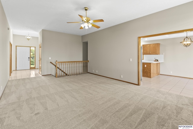 unfurnished room featuring baseboards, light carpet, ceiling fan with notable chandelier, and light tile patterned flooring