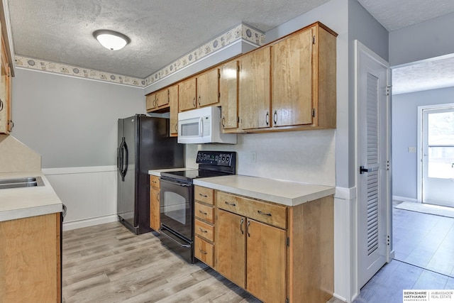kitchen with light countertops, a textured ceiling, black appliances, and light wood-style floors