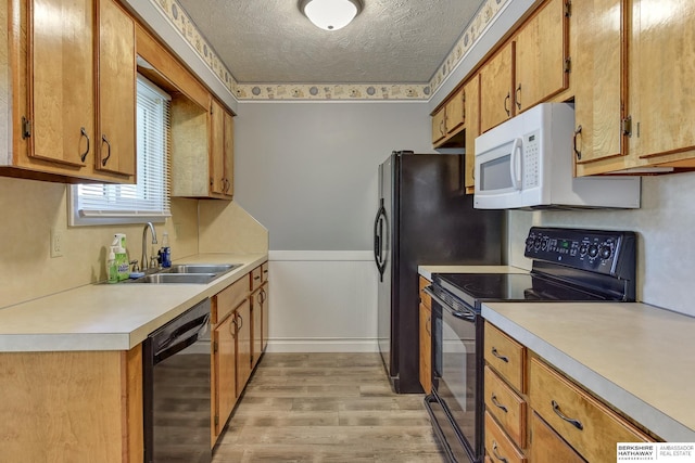 kitchen with a sink, light wood-style floors, light countertops, a textured ceiling, and black appliances