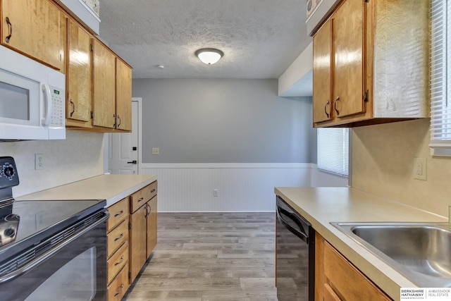 kitchen with wainscoting, a sink, light countertops, light wood-type flooring, and black appliances