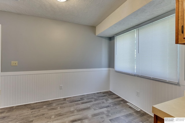 unfurnished room featuring wood finished floors, a wainscoted wall, and visible vents
