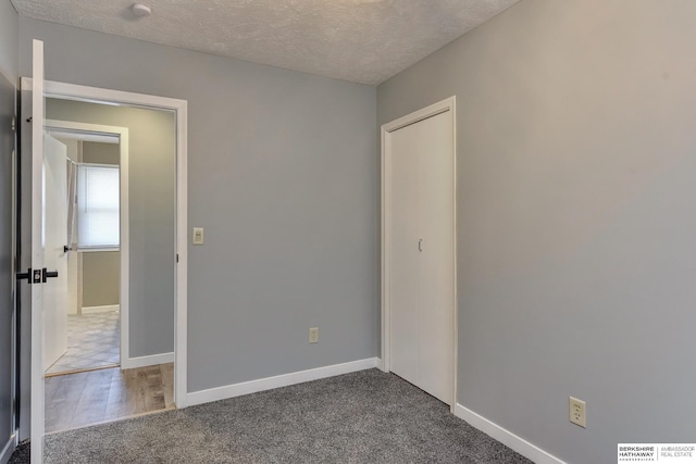 unfurnished bedroom featuring baseboards, a closet, dark carpet, and a textured ceiling