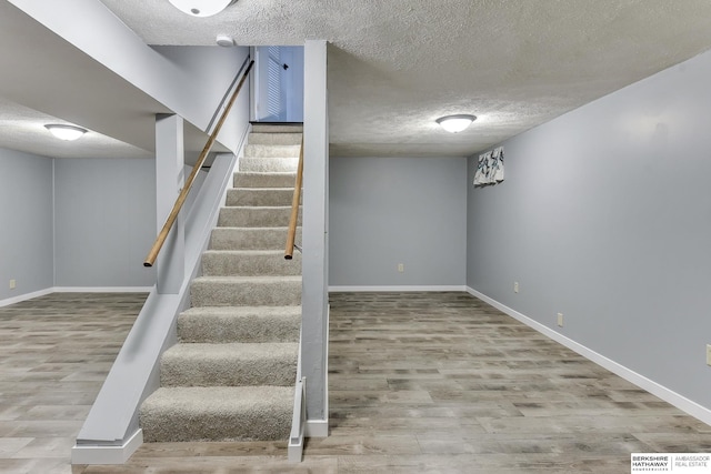 staircase featuring baseboards, a textured ceiling, and wood finished floors