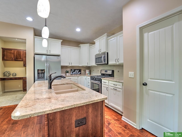 kitchen with appliances with stainless steel finishes, a sink, a kitchen island with sink, white cabinetry, and wood finished floors