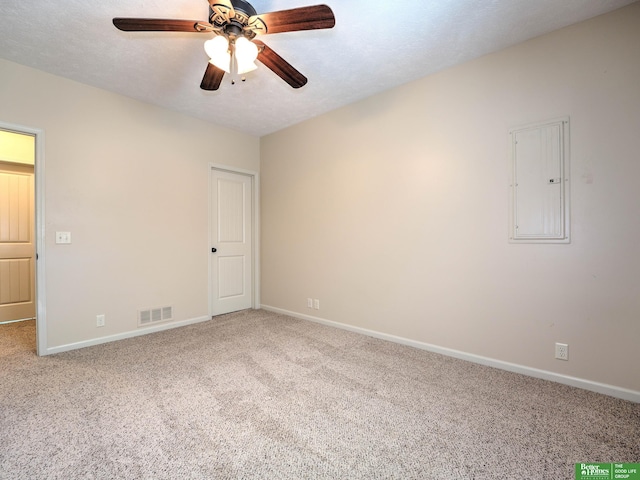 carpeted spare room featuring baseboards, ceiling fan, electric panel, and visible vents