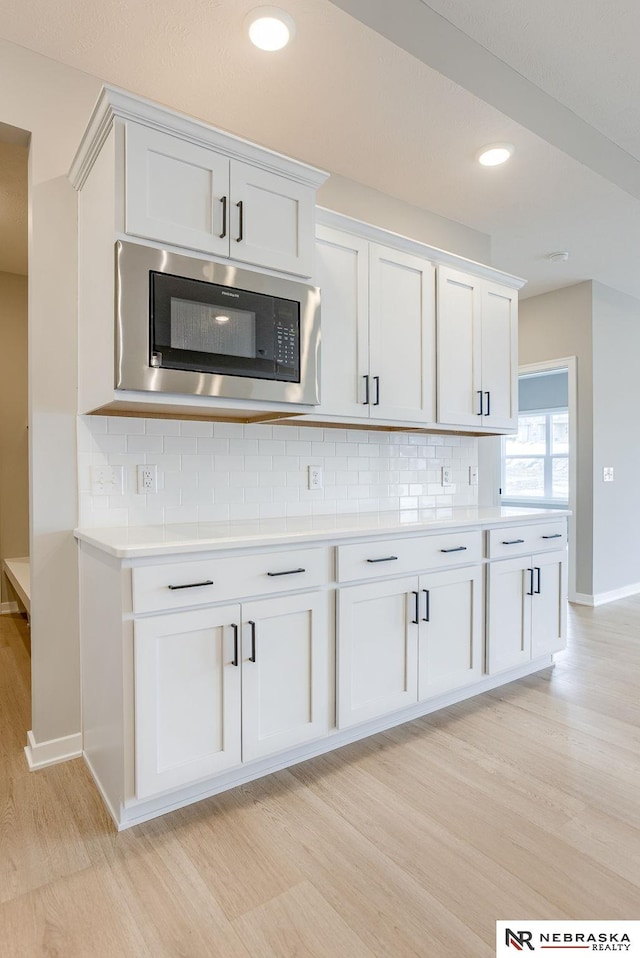 kitchen featuring backsplash, built in microwave, light countertops, white cabinets, and light wood-style flooring