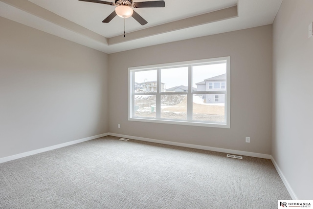 carpeted spare room with visible vents, a ceiling fan, a raised ceiling, and baseboards