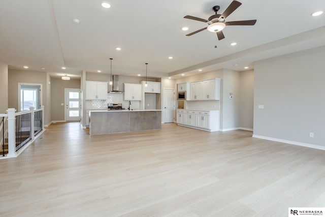 unfurnished living room featuring recessed lighting, a ceiling fan, a sink, and light wood finished floors