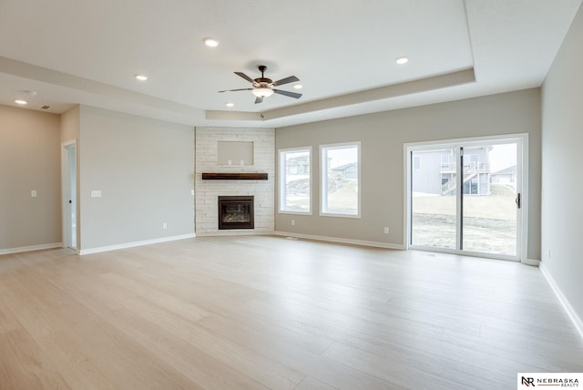 unfurnished living room featuring recessed lighting, light wood finished floors, ceiling fan, and a tray ceiling