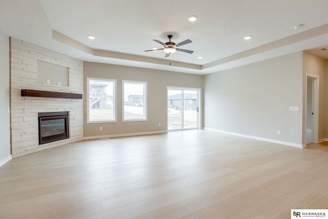 unfurnished living room with light wood-style flooring, a raised ceiling, ceiling fan, and a fireplace