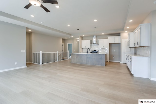 kitchen featuring a sink, open floor plan, wall chimney range hood, and tasteful backsplash