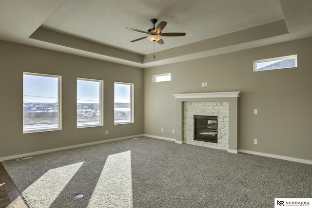 unfurnished living room featuring a glass covered fireplace, baseboards, ceiling fan, a tray ceiling, and carpet