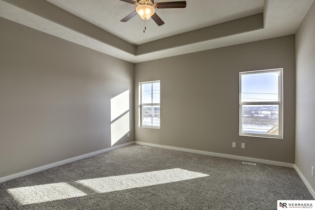 carpeted spare room featuring a tray ceiling, baseboards, a ceiling fan, and a wealth of natural light