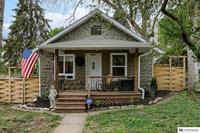 bungalow-style house featuring fence, a porch, and stone siding