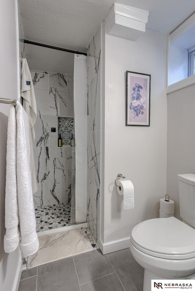 full bathroom with a marble finish shower, baseboards, toilet, and a textured ceiling