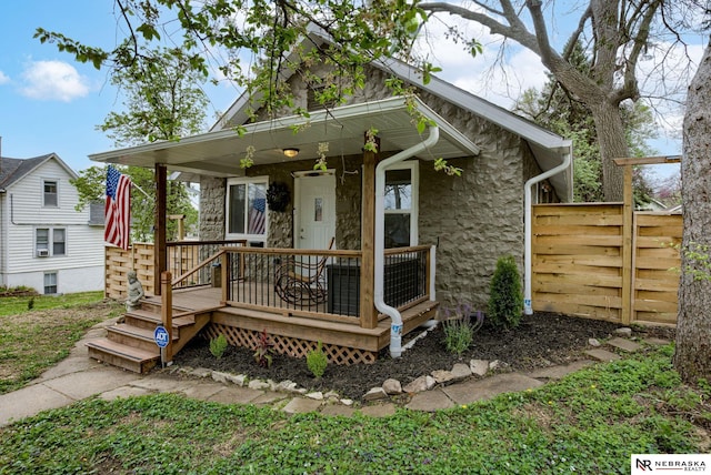 view of front facade with a porch, fence, and stone siding