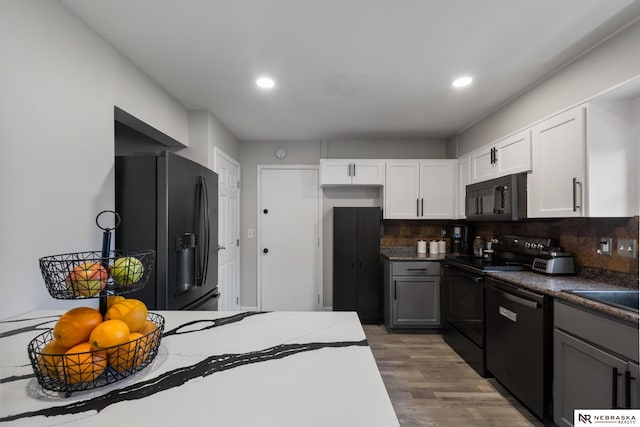 kitchen with wood finished floors, dark stone counters, white cabinets, backsplash, and black appliances