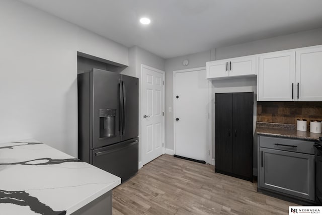 kitchen with light wood-style floors, light stone countertops, refrigerator with ice dispenser, and white cabinetry
