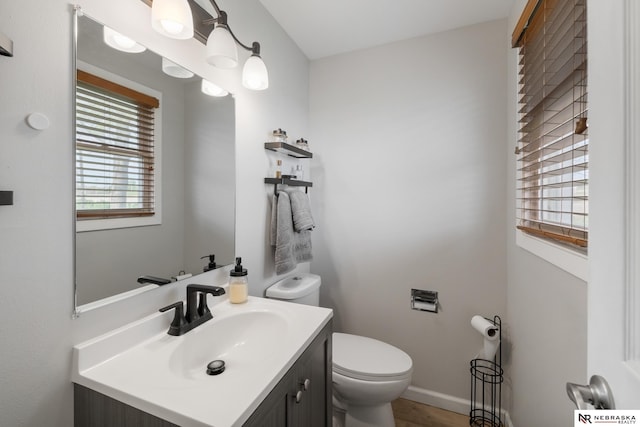 half bathroom with vanity, a healthy amount of sunlight, and toilet