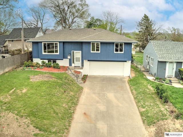 bi-level home featuring a garage, a front lawn, fence, a shingled roof, and concrete driveway