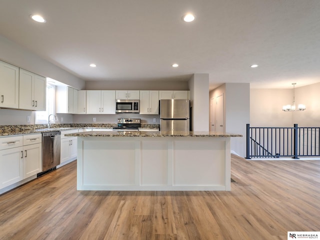 kitchen with a center island, stone counters, light wood-style floors, stainless steel appliances, and white cabinetry